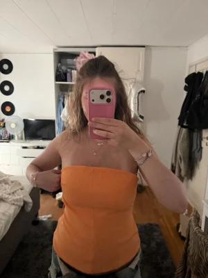 Orange bandeau tubtopp  - Snygg orange bandeau tubtopp öppen i ryggen och knappdetalj upptill. Toppen är ärmlös och croppad, perfekt för varma dagar. 