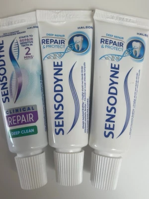 Sensodyne tandkräm tuber - Tre tuber Sensodyne tandkräm i vitt med blå och lila detaljer. Två av tuberna är märkta 'Repair & Protect' och en är 'Clinical Repair Deep Clean'. Tubernas material är plast och de har skruvkorkt.