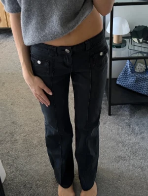 Svarta jeans med raka ben - Säljer ett par svarta jeans med raka ben och dekorativa sömmar framtill. Jeansen har fickor med lock och silverfärgade knappar fram. Snygg passform och klassisk look som funkar till det mesta. Perfekta för dig som gillar stilrena och trendiga jeans.