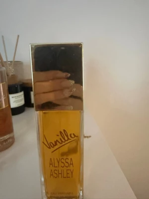 Alyssa Ashley Vanilla parfym 100ml - Alyssa Ashley Vanilla Eau Parfumée Cologne Spray i en rektangulär glasflaska med guldfärgat lock. Doften har en tydlig vaniljkaraktär och flaskan rymmer 100 ml. Stilen är enkel men lyxig med tydlig logga och gul text.