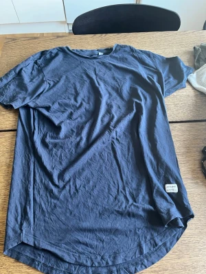 Mörkblå t-shirt från Jack & Jones - En stilren mörkblå t-shirt från Jack & Jones med rund halsringning och korta ärmar. T-shirten har en liten vit logotyp-patch nertill och är tillverkad i mjuk bomull. Perfekt för en avslappnad look.