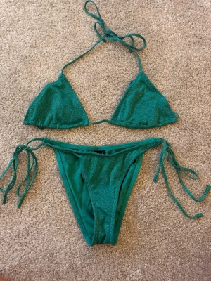 Triangl bikini - Snygg grön bikini med glittrigt tyg och klassisk trekantsmodell. Både överdel och underdel har knytband för justerbar passform. Perfekt för sommardagar på stranden eller vid poolen. Från märket triangl