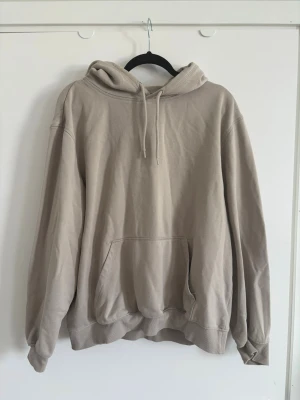 Beige oversized hoodie med huva - Säljer en beige oversized hoodie med huva och känguruficka framtill. Hoodien har dragsko i huvan och ribbade muddar vid ärmslut och nederkant. Perfekt för en avslappnad och stilren look.