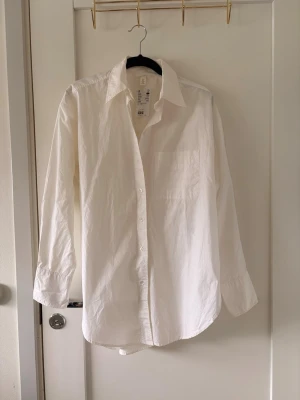 Vit klassisk skjorta från h&m  - Stilren vit skjorta från h&m med klassisk krage och bröstficka. Skjortan har lång ärm, knappar framtill och är tillverkad i mjuk bomull. Perfekt för en clean och enkel look.