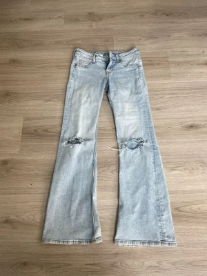 Ljusblå lågmidjade bootcutjeans med hål - Säljer ett par ljusblå bootcut jeans med hål på båda knäna. Säljer pågrund av att de är för små för mig.