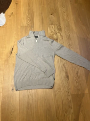 Beige stickad halvzip-tröja - Snygg beige stickad tröja med halv dragkedja i halsen. Tröjan har långa ärmar och ribbade muddar vid ärmslut och nederkant. Perfekt för lager-på-lager och enkel att matcha med olika outfits.