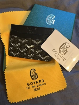 G plånbok - Säljer en elegant svart plånbok i klassisk design med ikoniskt mönster. Perfekt för dig som vill ha en lyxig men diskret accessoar till vardags.  Plånboken är helt ny och oanvänd, i toppskick. Smidig storlek men med plats för kort och sedlar.