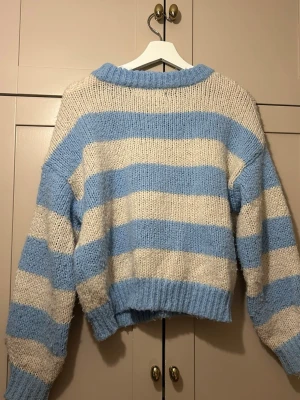Blåvit randig stickad tröja Vero Moda - mysig stickad tröja från Vero Moda med breda blå och vita ränder. Tröjan har en avslappnad passform, ribbstickad halsringning, ärmslut och nederkant🩵🤍🩵🤍