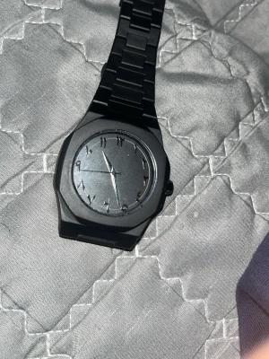 Svart stilren klocka med metallarmband - Snygg svart klocka med minimalistisk design och mattsvart urtavla. Klockan har ett robust metallarmband och stilrena arabiska siffror på urtavlan. Perfekt accessoar för en modern look.
