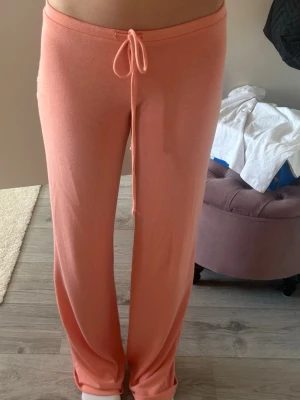 Coral mjukisbyxor från Nelly  - Säljer ett par persikofärgade mjukisbyxor med raka ben och dragsko i midjan. Byxorna är i ett mjukt och stretchigt material, perfekta för chill dagar hemma. Ingen synlig logga eller märke.