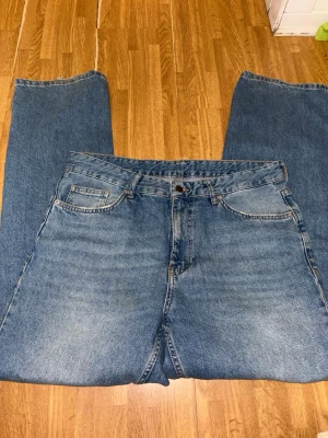 Blå raka jeans i klassisk modell - berska - Ett par blå jeans med rak passform och fem fickor. Jeansen har en klassisk denimtvätt och subtila slitningar framtill. Tillverkade i bomull med traditionell knappgylf och bälteshällor. Perfekta för en avslappnad och tidlös stil. Be om mått för det står ingen storlek på den!