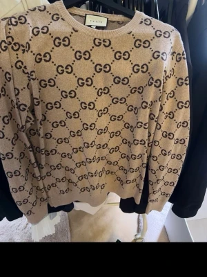 Beige stickad tröja från Gucci - Äkta sweatshirt ifrån Gucci ni kan även skicka den till verifierings centralen innan ni får tröjan. Snygg beige stickad tröja från Gucci med det klassiska GG-mönstret i mörkbrunt över hela plagget. Rund halsringning och ribbade muddar vid ärmslut och nederkant. Perfekt för dig som gillar lyxiga och trendiga plagg. Tröjan går för cirka 8300 på affär,  Pris kan diskuteras så tveka inte på att höra av er