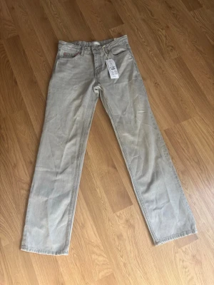 Grå raka jeans från Gina tricot  - Snygga grå jeans från Gina  med rak passform och klassisk femficksdesign. Jeansen har hög midja och är tillverkade i ett kraftigt bomullstyg. Perfekta för en clean och avslappnad stil.