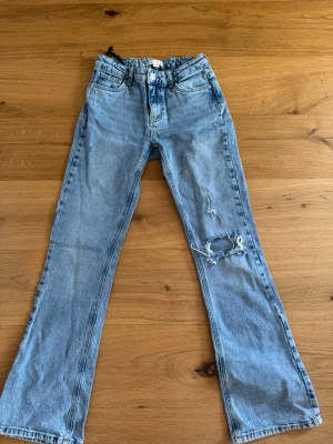 Ljusblå jeans med hål Gina Tricot - Säljer ett par ljusblå jeans från Gina Tricot x Iza & Elle , med bootcut och slitningar på ena benet. Bra skick , storlek 158
