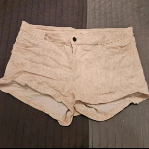 Shorts H&M 44 - Snygga beige shorts med diskret mönster och klassisk femficksdesign. De har bälteshällor och stängs med knapp och dragkedja. Perfekta för sommardagar och lätta att matcha med olika toppar  Kan även hämtas I Partille  E5