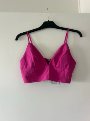 Rosa top med smala axelband - Trendig rosa linnetopp med smala axelband och v-ringad skärning. Toppen har en croppad passform och är perfekt för att styla med höga jeans eller kjol. Enkel och stilren design som ger en fräsch look.