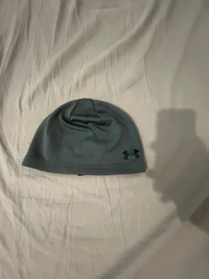 Grå mössa från Under Armour - Snygg grå mössa från Under Armour med diskret logga framtill. Tillverkad i ett stretchigt och mjukt material som sitter skönt på huvudet. Perfekt för dig som vill ha en enkel och sportig look.