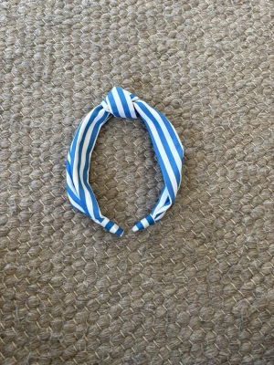Blåvitt randigt diadem med knut - Snyggt diadem med blå och vita ränder och en knut på toppen. Diademet har en klassisk form och är tillverkat i ett mjukt tygmaterial som är bekvämt att bära. Perfekt för att ge din look en fräsch touch.