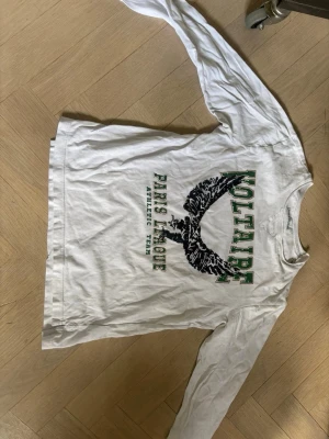 Vit långärmad topp Zadig & Voltaire - Vit långärmad topp från Zadig & Voltaire med tryck i grönt och svart framtill. Rund halsringning och avslappnad passform. Tillverkad i mjuk bomull, perfekt för en cool och avslappnad stil.