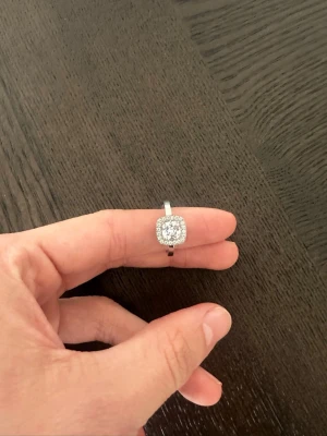 Edblad ring - Stilren silverfärgad ring med fyrkantig front dekorerad med små gnistrande stenar i två rader runt en större mittsten. Ringen har en klassisk och elegant design som verkligen fångar blicken.