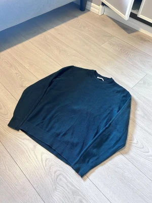 Mörkgrön stickad tröja från Zara - Säljer en mörkgrön stickad tröja från Zara med rund halsringning och ribbade muddar. Tröjan har en enkel och stilren design, perfekt för dig som gillar klassiska plagg. Materialet är mjukt och bekvämt, och den har långa ärmar.