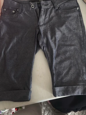 Mörkblå jeansshorts High Level - Snygga mörkblå jeansshorts från High Level med klassisk femficksdesign och uppvikta benslut. Shortsen har bälteshällor och knappstängning framtill. Perfekta för en avslappnad stil under varmare dagar.