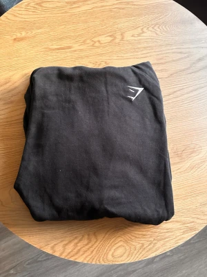 Svart hoodie från Gymshark - Svart hoodie från Gymshark med diskret logga på bröstet. Klassisk modell med huva och snörning samt en stor magficka. Perfekt för en avslappnad stil och passar bra till träning. Säljer den då jag beställde 2 och inte han skicka tillbaka den, tröjan är använd 1 gång ( pris ej hugget i sten)