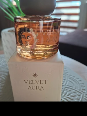 Velvet Aura Eau de Parfum Rituals - Velvet Aura Eau de Parfum från Rituals med en rund, transparent glasflaska och guldfärgad vätska. Flaskan har ett solmotiv och en matt, grå kork. Medföljer en elegant vit kartong med guldtext. Perfekt för dig som gillar lyxiga dofter.
