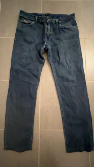 Mörkblå jeans från Hugo boss - Snygga mörkblå jeans från Hugo boss med klassisk femficksdesign och raka ben. Jeansen har en metallknapp och dragkedja framtill samt bälteshällor. Materialet är denim och färgen är djup blå, perfekt för en avslappnad look. Storlek 32:32 pris kan diskuteras vid snabb affär!