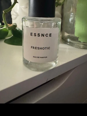 Essnce Freshotic Eau de Parfum - Essnce Freshotic Eau de Parfum i en stilren, cylindrisk glasflaska med svart lock. Parfymen har en transparent vätska och minimalistisk vit etikett med svart text. Perfekt för dig som gillar fräscha och moderna dofter. Ungefär 3/4 kvar kanske om inte mer🥰