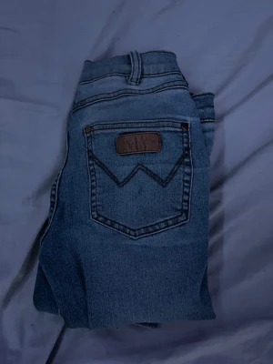 Wrangler blå raka jeans köpte från labelle o Karlsson  - Säljer ett par klassiska blå jeans från Wrangler med raka ben och ikoniska W-detaljer på bakfickorna. Jeansen har normalhög midja, bälteshällor och är tillverkade i slitstark denim. Perfekta för en avslappnad och tidlös stil.