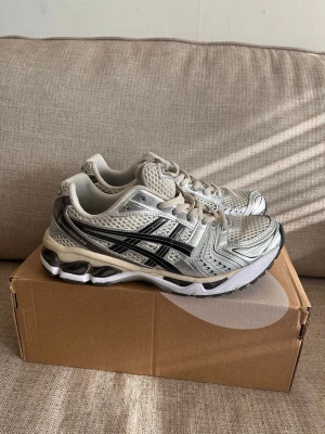 Ascona gel kayano - Snygga sneakers från ASICS i silver och vitt med svarta detaljer. Ovandelen är i mesh och syntet för bra andningsförmåga och komfort. Klassisk sportig design med tydliga ASICS-loggor på sidorna och tungan. Perfekta för en trendig och sportig look.