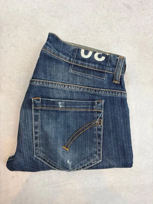 Blå jeans från Dondup med raka ben - Snygga blå jeans från JC med raka ben och klassisk femficksdesign. Jeansen har slitningar och ljusare partier framtill för en cool, använd look. Tydliga kontrastsömmar och JC-logga baktill i midjan. Perfekta till vardagsstilen!