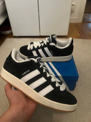Adidas Campus 00s svarta  - Säljer ett par Adidas Campus 00s i klassisk svart/vit färg med gum sole. Väldigt stilrena och enkla att matcha till allt.  Skick: mycket bra, sparsamt använda Storlek: EU 44 / US 10 Originalbox ingår Extra svarta skosnören ingår  Snabb frakt 🚚frågor? DM