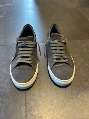 Mörkgrå mocka sneakers - Snygga mörkgrå sneakers i mocka med vita sulor och klassisk snörning. Skorna har en stilren design och passar perfekt till streetwear eller casual outfits. Bekväm passform och diskret look som funkar till det mesta.