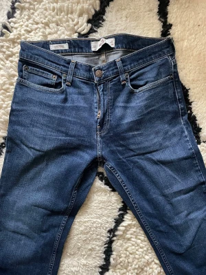 Mörkblå raka jeans från Hollister - Snygga mörkblå jeans från HOLLISTER med klassisk femficksmodell och raka ben. Jeansen har en diskret tvätt och är tillverkade i bomull med en liten stretch för extra komfort. Perfekta för en stilren och avslappnad look.