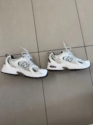 Vita New Balance 530 sneakers - Snygga New Balance 530 sneakers i vitt med silver- och gråa detaljer. Skorna har meshpaneler för extra andningsförmåga och klassisk N-logga på sidorna. Sulan är vit med svarta och grå inslag. Perfekta för en sportig och trendig look. Endast andvända i en vecka.