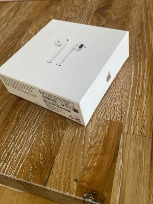 Apple AirPods trådlösa hörlurar - Säljer ett par vita Apple AirPods med laddningsetui. De är trådlösa in-ear hörlurar i stilren och minimalistisk design, tillverkade i plast. Perfekta för musik, samtal och smidig anslutning till iPhone och andra Apple-enheter.