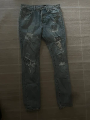 Denim slitna jeans  - Säljer ett par ljusblå jeans med slitningar. Jeansen har klassisk femficksmodell och raka ben. Perfekta för dig som gillar en avslappnad och trendig streetstil.