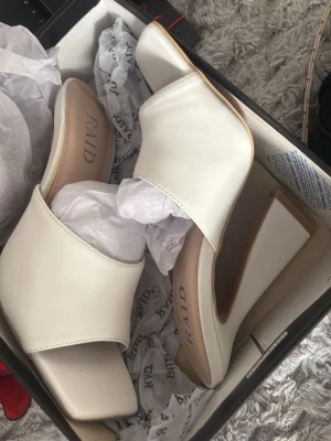 Vita slip-in pumps från RAID - Stilrena vita slip-in pumps från RAID med fyrkantig tå och bred klack. Skorna har en minimalistisk design och är tillverkade i ett slätt material som ger en modern look. Perfekta för dig som gillar trendiga och bekväma klackar.