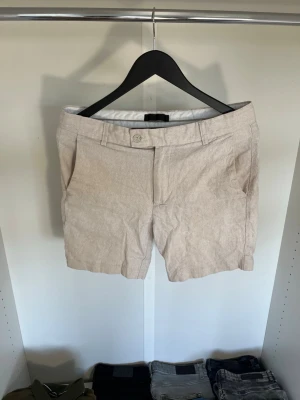 Beige linneshorts från KIOMI - Snygga beige shorts från KIOMI i linne med klassisk passform. De har knapp och dragkedja framtill, bälteshällor och sidofickor. Hör gärna av dig vid frågor!
