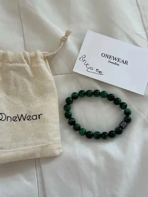 Grönt pärlarmband från OneWear - Snyggt armband från OneWear med runda gröna pärlor och en svart detalj. Armbandet är elastiskt och levereras med tygpåse och kort. Perfekt accessoar för att lyfta din stil.