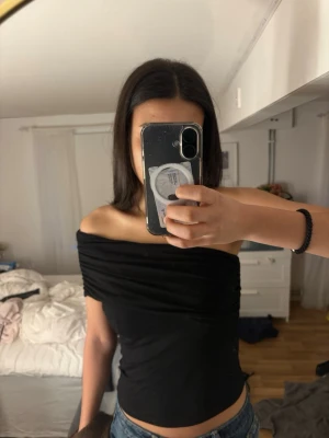 Svart offshoulder topp - Snygg svart offshoulder topp med tight passform och rynkade detaljer vid axlarna. Perfekt att styla med jeans eller kjol för en trendig look. Mjuk och stretchig känsla, passar dig som gillar minimalistisk stil.