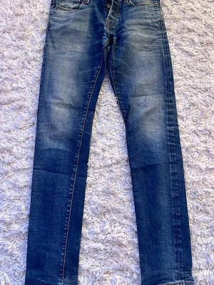 Mörkblå slim fit jeans med slitningar - Snygga mörkblå slim fit jeans med lätt slitna detaljer och klassisk femficksdesign. Jeansen har en något tvättad look och raka ben. Perfekta för en avslappnad och trendig stil. Materialet är troligtvis bomull med stretch för extra komfort.