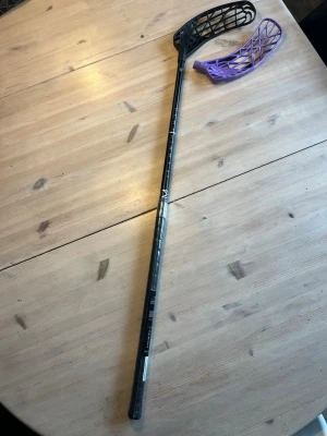Oxdog playlight 27 med extra blad - Säljer en svart innebandyklubba med ett extra lila blad. Klubban har ett modernt utseende och är tillverkad i lätt material, perfekt för snabba spel. Bladen är i plast och klubban har tryck i vitt längs skaftet. 