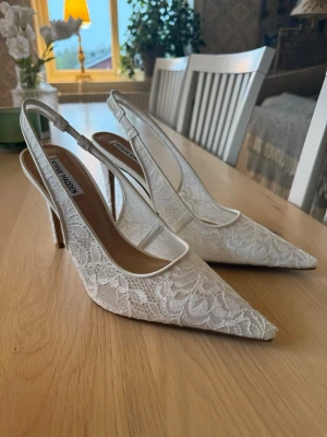Vita spets klackar från Steve Madden - Snygga vita klackar från Steve Madden med spetsig tå och smal klack. Skorna har ett elegant spetsmönster och öppen häl. Aldrig använda, säljer för att det inte går att skicka tillbaka och dom var för stora. Klacken är 10cm hög. Kommer i orginalförpackning. Pris kan diskuteras 