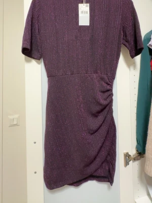 Glittrig lila kortklänning från Mango - Snygg lila kortklänning från Mango med glittriga inslag och lätt rynkade detaljer på sidan. Helt ny, oanvänd 💜 Skickar gärna fler bilder om det behövs :)