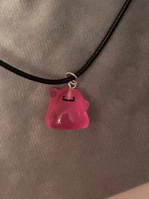 Självlysande Ditto halsband Pokémon smycke  - Så gulligt halsband med en berlock av Ditto!Berlocken är ca 1,5 x 1,5 cm och trädd på svart tråd. Den är också självlysande och lyser i mörkret. Halsbandet är justerbart 40-45 cm. 