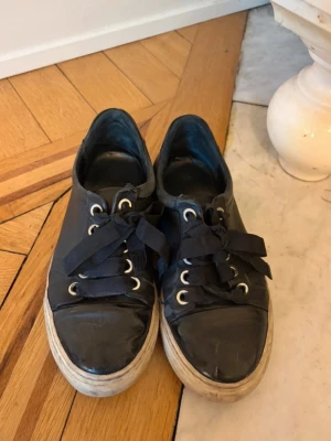 Svarta låga sneakers med vita sulor - Snygga svarta sneakers med lågt skaft och vita, tjocka sulor. Skorna har svarta skosnören och metallfärgade öljetter. Från Billi Bi Copenhagen.