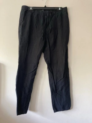 Svarta linnebyxor med dragsko - Snygga svarta linnebyxor med avslappnad passform och dragsko i midjan. Byxorna har sidofickor och en bakficka, perfekta för en chill och stilren look. Tillverkade i luftigt linne som passar perfekt till varmare dagar.